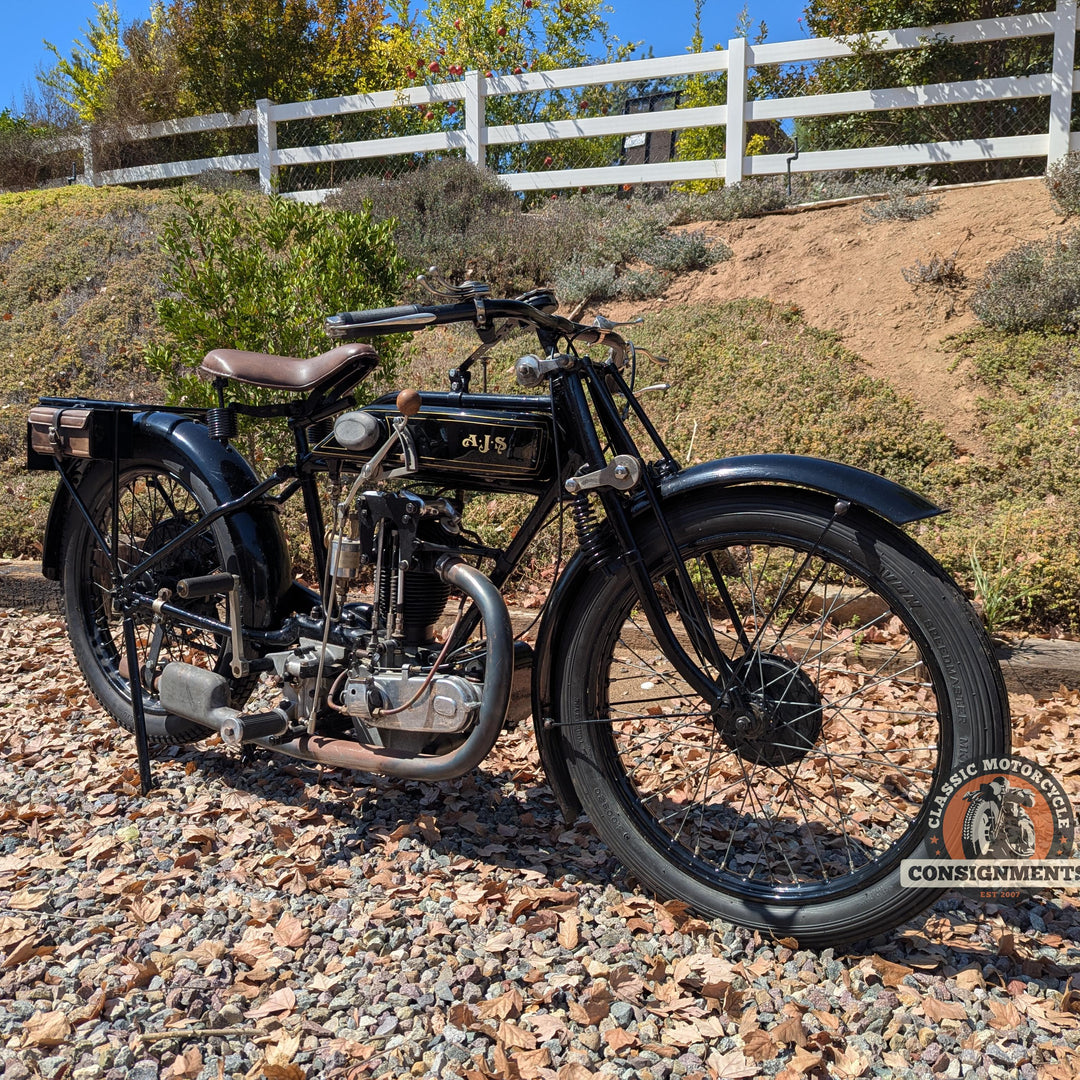Vintage motorcycle on a gravel path with a white fence and trees in the background