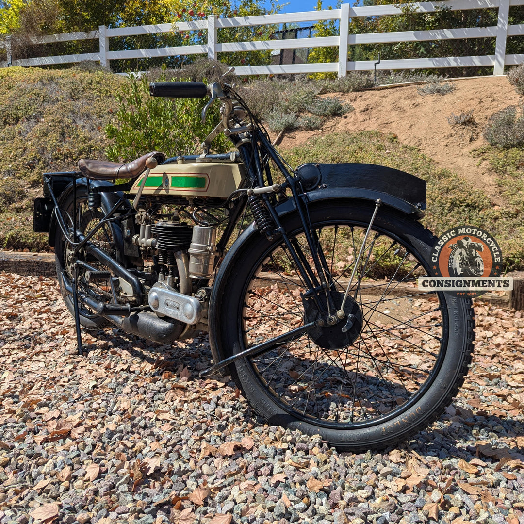 Vintage motorcycle on a gravel surface with a white fence and greenery in the background